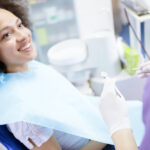 Black woman smiles while sitting in a dental chair looking at her dentist