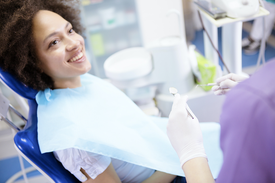 Black woman smiles while sitting in a dental chair looking at her dentist