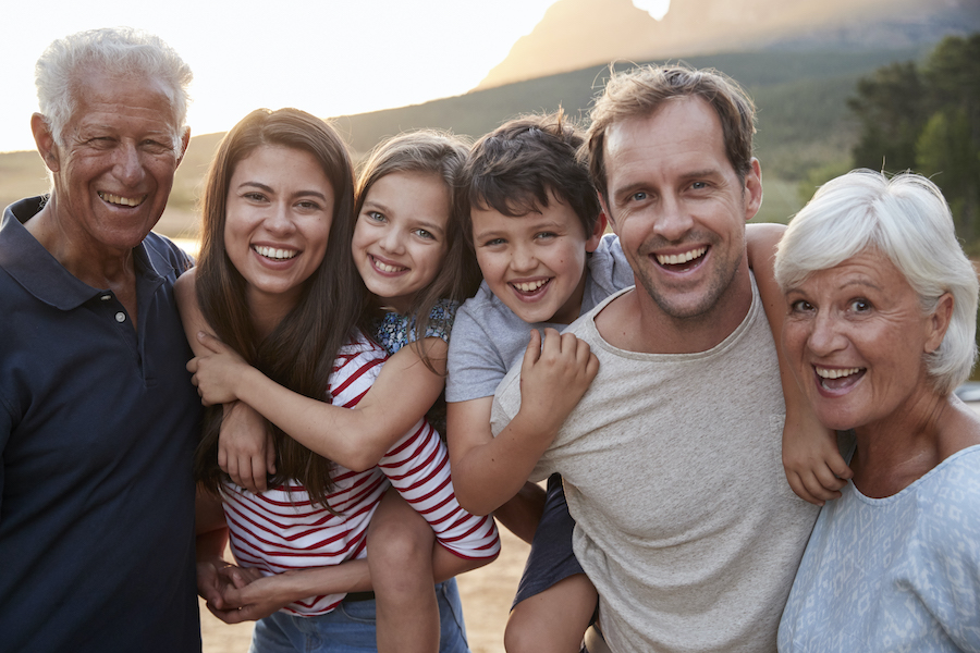 Multigenerational family of grandparents, parents, and 2 children smiling outside. Accompanies article about how family dentists can help with dental anxiety.