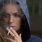 woman wearing a hooded jacket smokes a cigarette