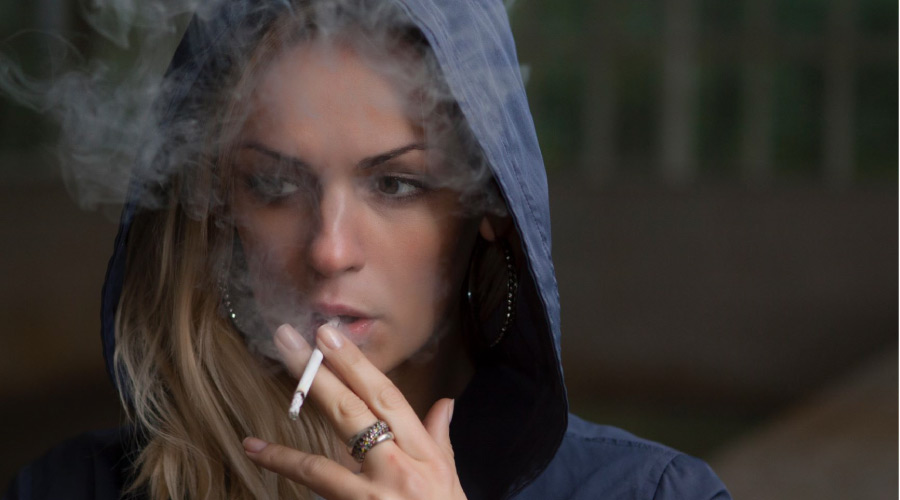 woman wearing a hooded jacket smokes a cigarette
