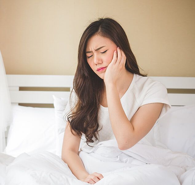 woman sitting up in bed, holding her jaw in pain